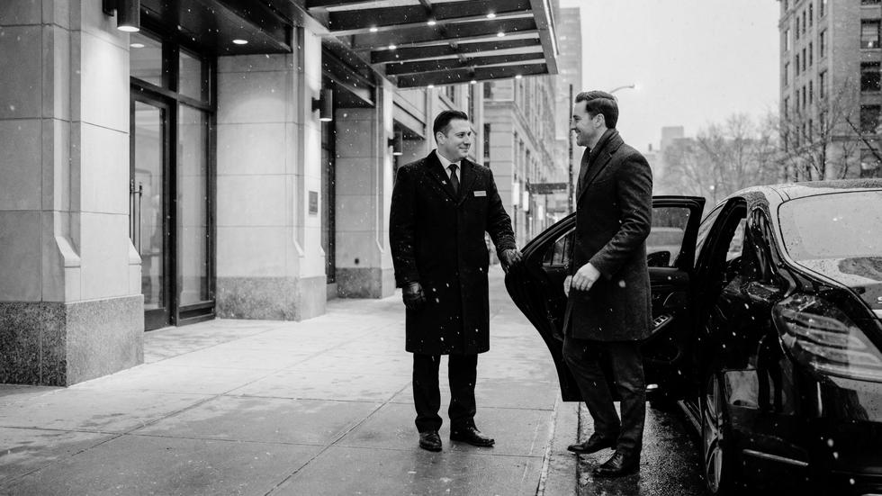 Professional valet greeting a guest outside a luxury building during winter, highlighting refined arrival service and first impressions in cold weather conditions.