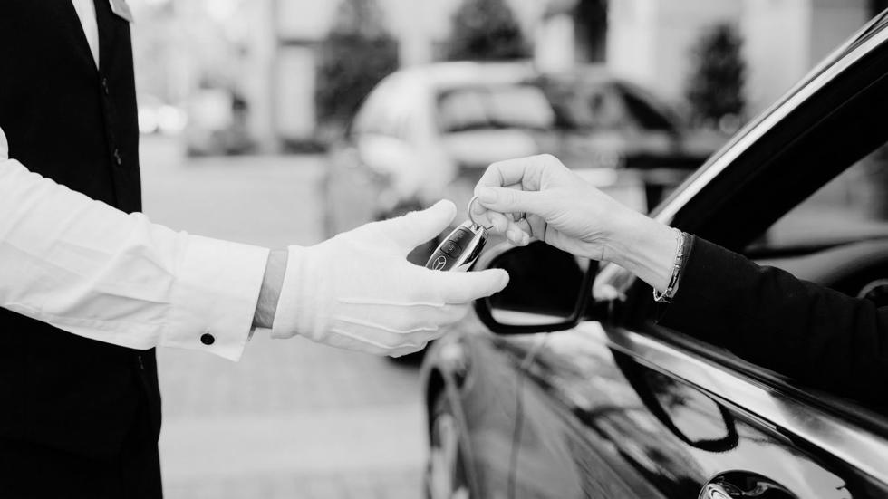 Customer handing car keys to a professional valet attendant wearing white gloves during a premium valet parking service.