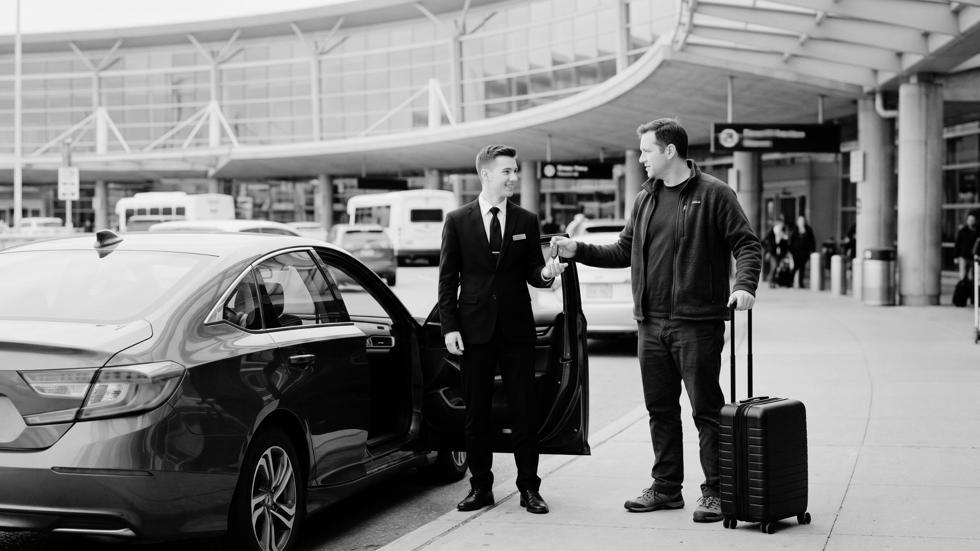 Valet attendant receiving car keys from a traveler with luggage at an airport terminal in Toronto, illustrating convenient airport valet parking service during departure drop-off.