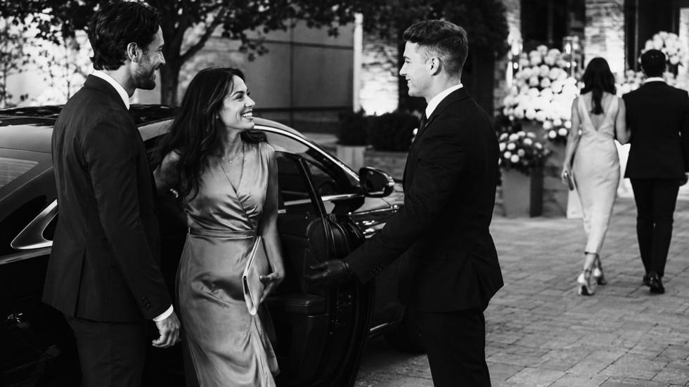 Valet attendant greeting smiling wedding guests as they step out of a luxury vehicle outside an upscale Toronto wedding venue, showcasing professional valet service and a refined guest experience.